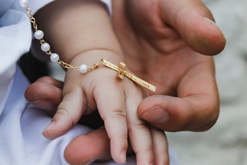 man holding baby's hand with a baptism rosary