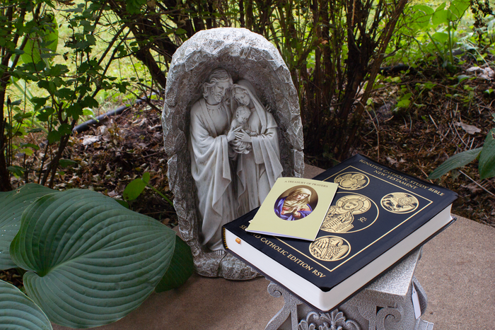 An outdoor sacred space featuring a Holy Family shrine, a prayer booklet, and a  leather bound Bible.